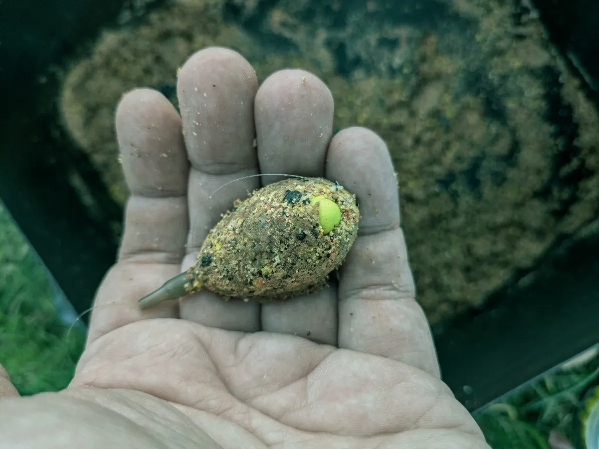 Een method feeder vol voer met een gele wafter erin gedrukt, in de hand boven de voerbak